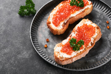 Two dandwiches with red caviar. Salmon red caviar in bowl and sandwiches server on old iron plate on old black table background. Top view. Copy space.