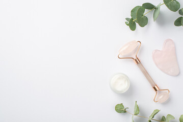 Top view photo of eucalyptus cream bottle rose quartz roller and gua sha on isolated white...