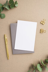 Business concept. Top view vertical photo of paper card grey envelope gold pen binder clips and eucalyptus on beige background with blank space