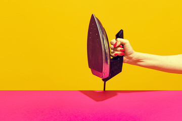 Colorful bright image of female hand holding retro iron isolated over pink yellow background