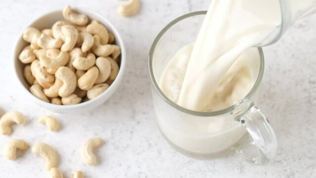 Slow motion of pouring vegan cashew milk in a glass. Alternative lactose free nut milk