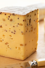 Piece of Belgian cheese with mustard seed and Fenugreek on a cutting board close up    