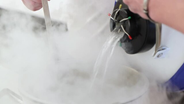 People are working with liquid nitrogen. A man is pouring nitrogen from special container into steel saucepan, close-up 4k video