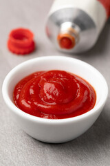 Bowl with tomato ketchup close up and a tube of tomato ketchup in the background   
