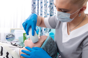 Young woman receiving electric galvanic anti-aging face spa massage at beauty salon.