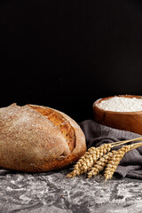 Rustic sourdough bread, golden spikelets of wheat and flour on a black background, vertical frame