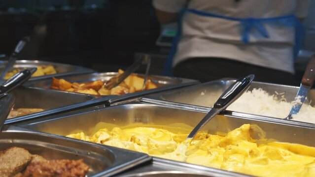 a sales assistant in a supermarket cookery puts a portion of meat in a yellow cheese sauce into a pasty food container. Food to go