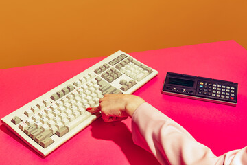Colorful image of female hand typing on retro computer keyboard isolated over pink orange background