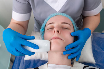 Young woman receiving electric galvanic anti-aging face spa massage at beauty salon.