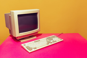 Colorful image of vintage computer monitor and keyboard on bright pink tablecloth over yellow...