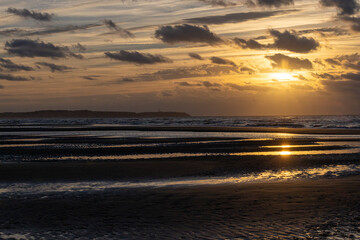 A beautiful, dramatic golden- sunset with some small dark clouds over a beautiful French beach with some small waves rolling in at the shore. High quality photo