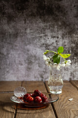 Cherry jam in a plate on a wooden table with a branch of cherry flowers in a vase.