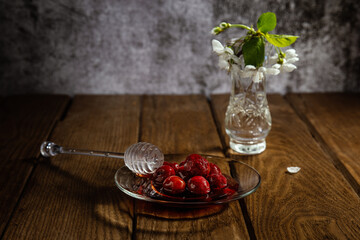 Cherry jam in a plate on a wooden table with a branch of cherry flowers in a vase.
