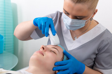 Young woman receiving electric galvanic anti-aging face spa massage at beauty salon.