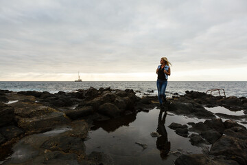 Women on volcanic rocks and blue ocean with waves, white foam and volcanic rocks. Canary Islands. The magnificent coast of the Atlantic Ocean