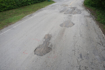 The road is full of holes and potholes. The old asphalt road surface is rough and bumpy and in need of repair. 