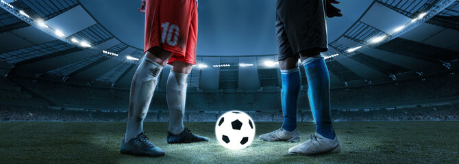 Night football match. Cropped image of two soccer, football players standing near luminous ball at stadium in evening. Concept of sport, competition, goals