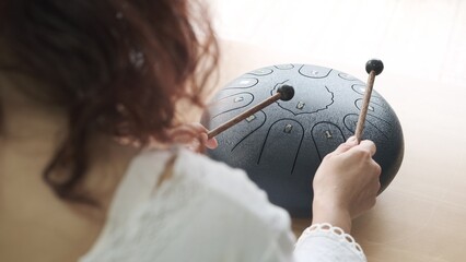 Asian woman playing steel tongue drum musical instrument on the table.