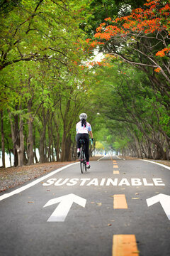Sustainable word with sportswoman ride bike on road with white arrow. Sustainability concept and development lifestyle idea