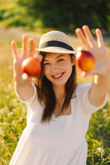 Happy carefree summer girl in outdoor field with orange peach fruit. Young woman eats peach. Summer picnic setting.