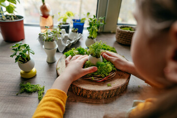 Little girl decorating nest with green moss on the table