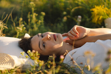 Beautiful romantic young woman lying on a blanket on a summer meadow. Time for yourself. Relaxing on summer meadow. A girl with beautiful hair is enjoying the summer weather.