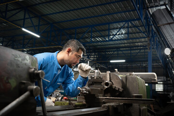 Selective focus of a professional Asian male lathe worker in a blue uniform and gloves, standing...