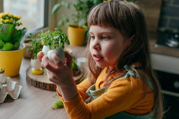 Little girl decorating eggshell with toy eyes on the table