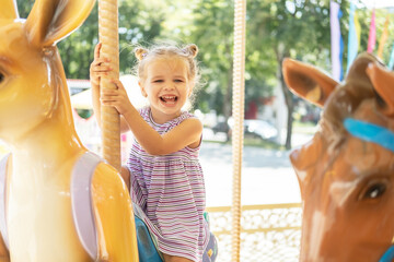 funny little kid girl in colorful dress rides on carousel in an amusement park in summer day © Юля Шевцова
