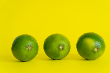 Ripe limes on yellow surface with copy space