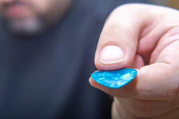 A musician in a dark T-shirt holds out a guitar pick forward. The man encourages people to learn to play the guitar.