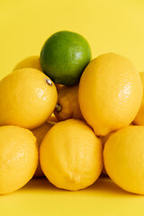 Close up view of green lime on lemons on yellow surface
