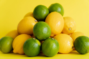 Juicy limes near heap of blurred lemons on yellow surface