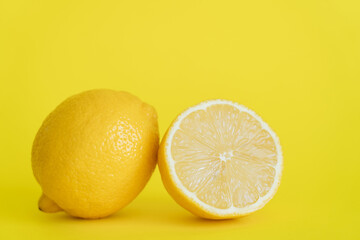 Close up view of half and whole lemon on yellow background