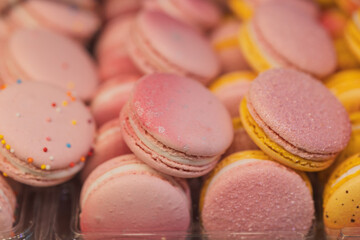 A lot of beautiful French sweets macaroons of yellow and pink colors with patterns lie in rows in assortment in a bakery