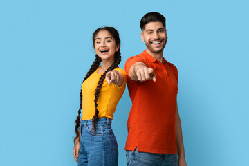 Positive young middle eastern man and woman pointing with fingers at camera