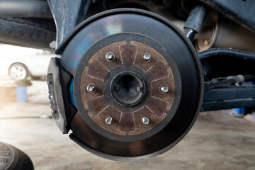 Maintenance background of car's suspension with the rear wheels removed reveals disc brakes.