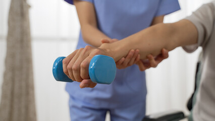 closeup shot hand of disabled person going through rehab training using a dumbbell. cropped female nursing aide provided assistance at background