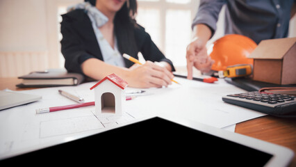 House model on table with group of two coworkers working with blueprint in office. co-working teamwork concept.