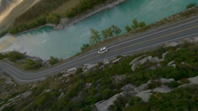 Aerial view mountain sunny valley minibus car riding on highway near river exploration travel. FPV sport drone close flight past a fir tree rocky organic environment fresh landscape tourism adventure