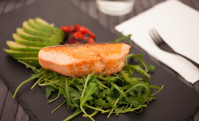 Baked sea trout fillet with fresh vegetables and herbs on black board