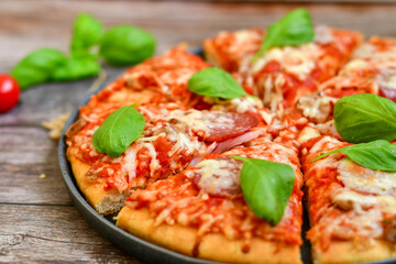  Close up of   classic  Italian Pizza   with Ham and salami . Fresh basil,tomato sauce ,mozzarella cheese , mushrooms and  green peppers