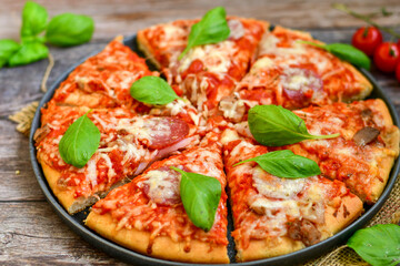  Close up of   classic  Italian Pizza   with Ham and salami . Fresh basil,tomato sauce ,mozzarella cheese , mushrooms and  green peppers