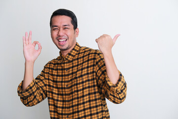 Adult Asian man smiling happy while pointing behind and give OK sign