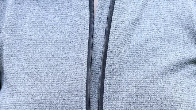 A woman's hand fastens and unzips a gray jacket on the street, put on a jacket, fasten the lock on clothes