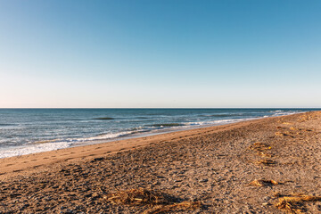 Uncrowded pebble beach at sunrise with cloudless blue sky in Motril, Andalusia Spain