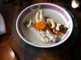 Chicken feet soup, hot and spicy  served in white bowl on wooden table. Known as sop ceker in Indonesia. Commonly mixed with vegetable such as carrot. Delicious, tasty, refreshing. Focus selection.