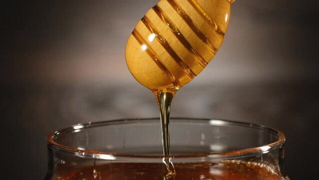 Honey in jar with honey dipper on rustic wooden background. Pouring into the jar. 4k footage