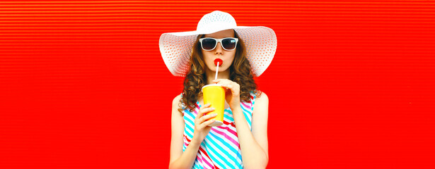 Portrait of beautiful young woman drinking fresh juice wearing summer hat on red background - obrazy, fototapety, plakaty