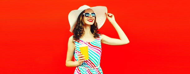 Portrait of happy smiling young woman with cup of juice looking away wearing summer hat on red background, blank copy space for advertising text